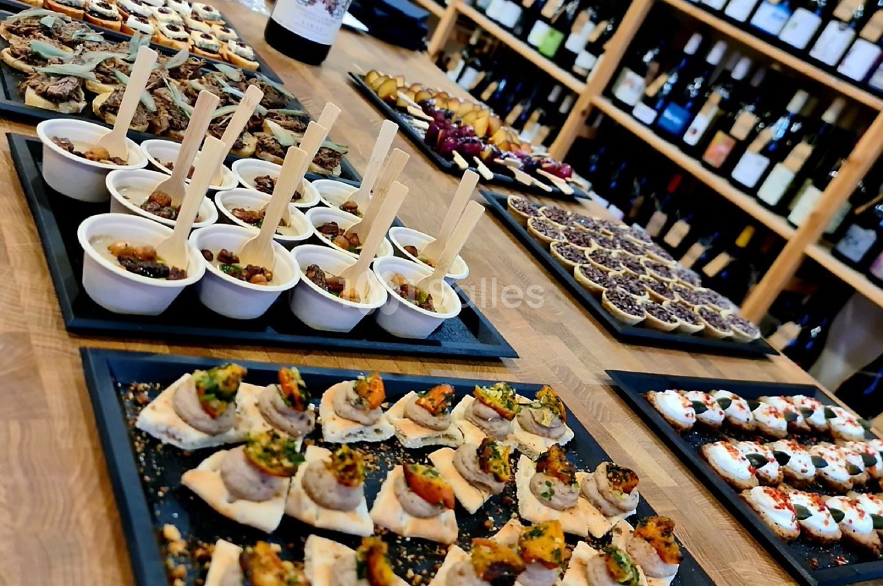 Plateaux de bouchées apéritives variées disposés sur une table en bois, avec des bouteilles de vin en arrière-plan.