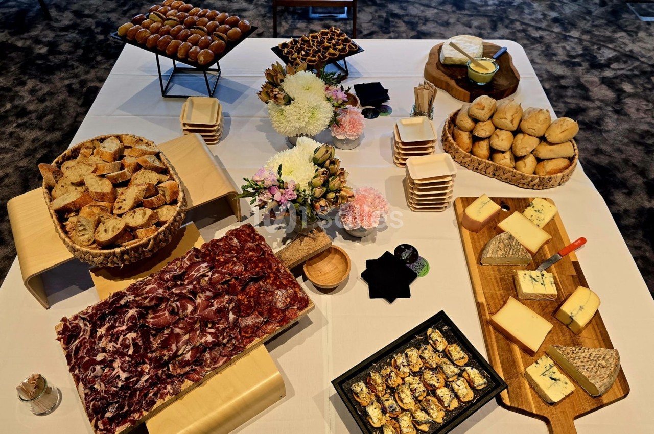 Table dressée avec charcuterie, fromages, pains variés, fleurs et petits plats pour un buffet ou une réception.