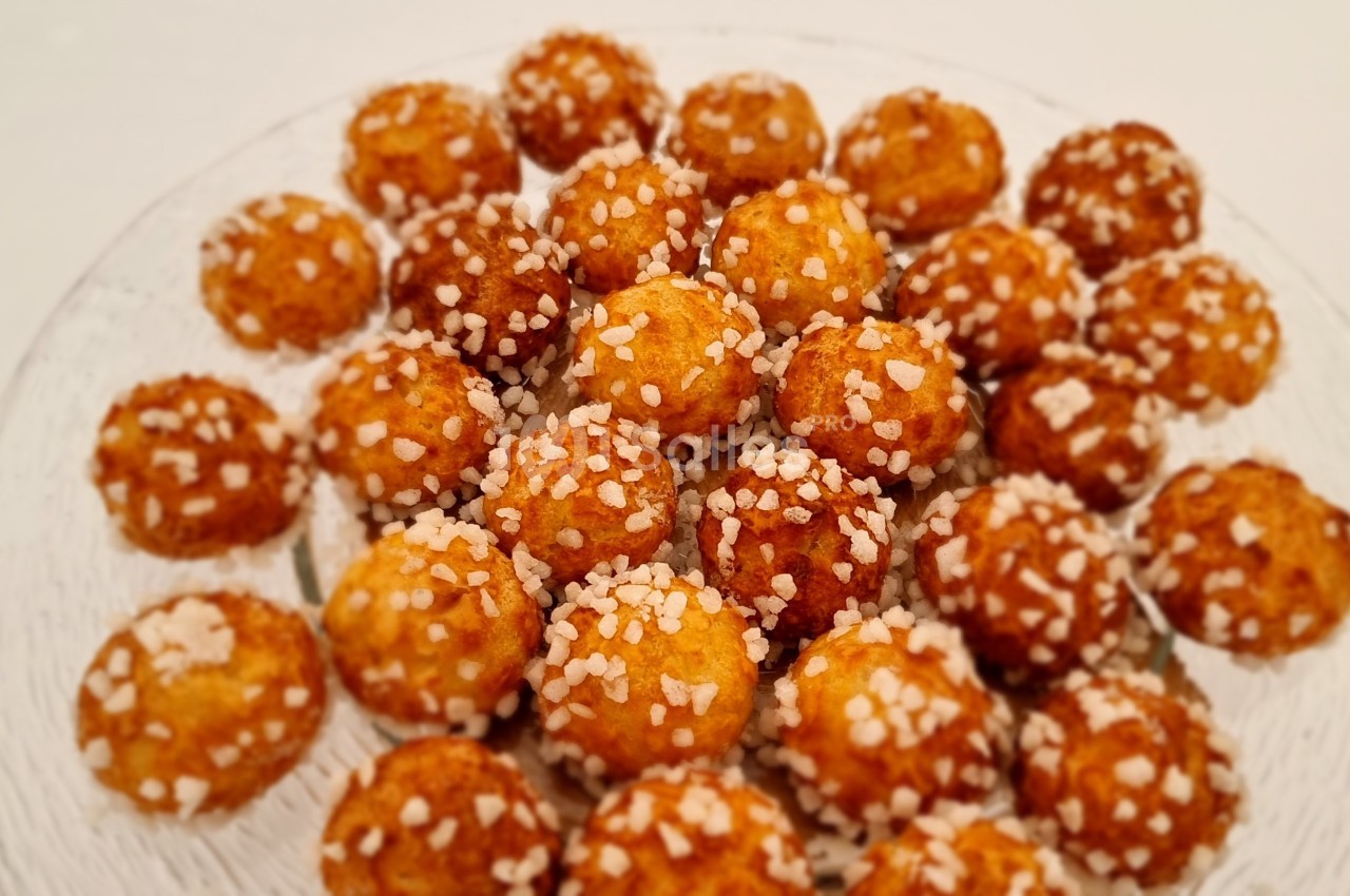 Assortiment de chouquettes dorées garnies de grains de sucre sur une assiette en verre.