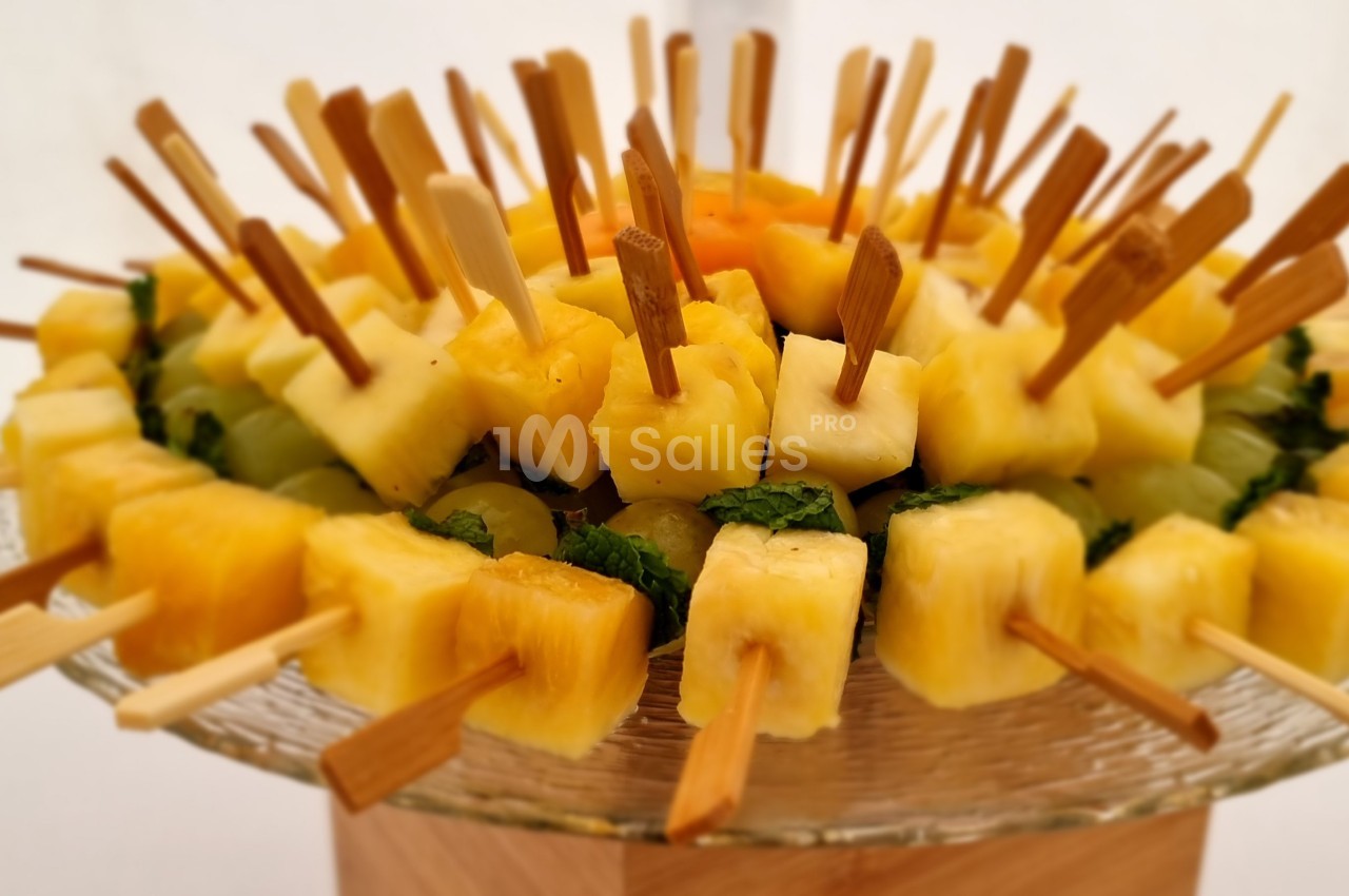 Brochettes de fruits composées d'ananas et de morceaux colorés, présentées sur un plat en verre.