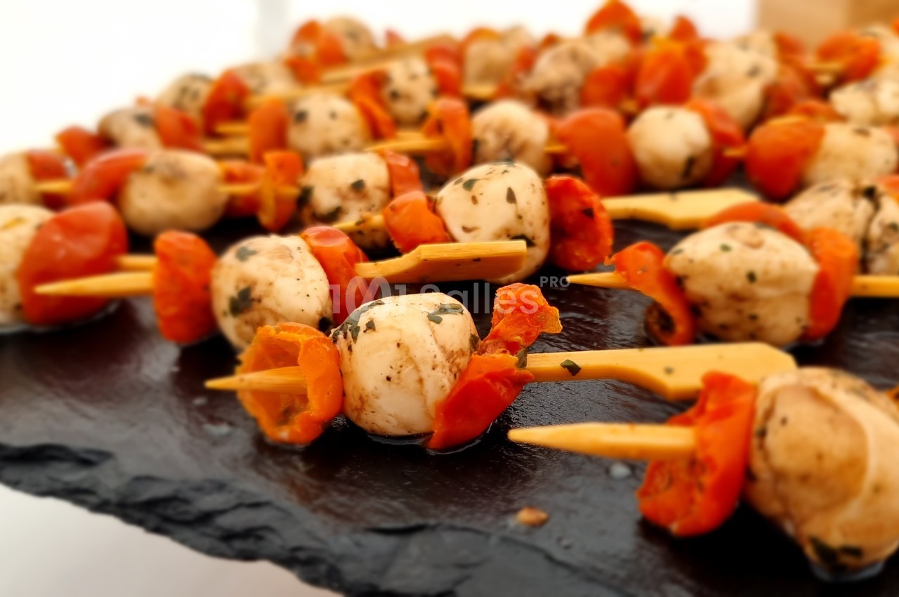 Brochettes apéritives composées de tomates cerises, champignons et épices, présentées sur une ardoise noire.