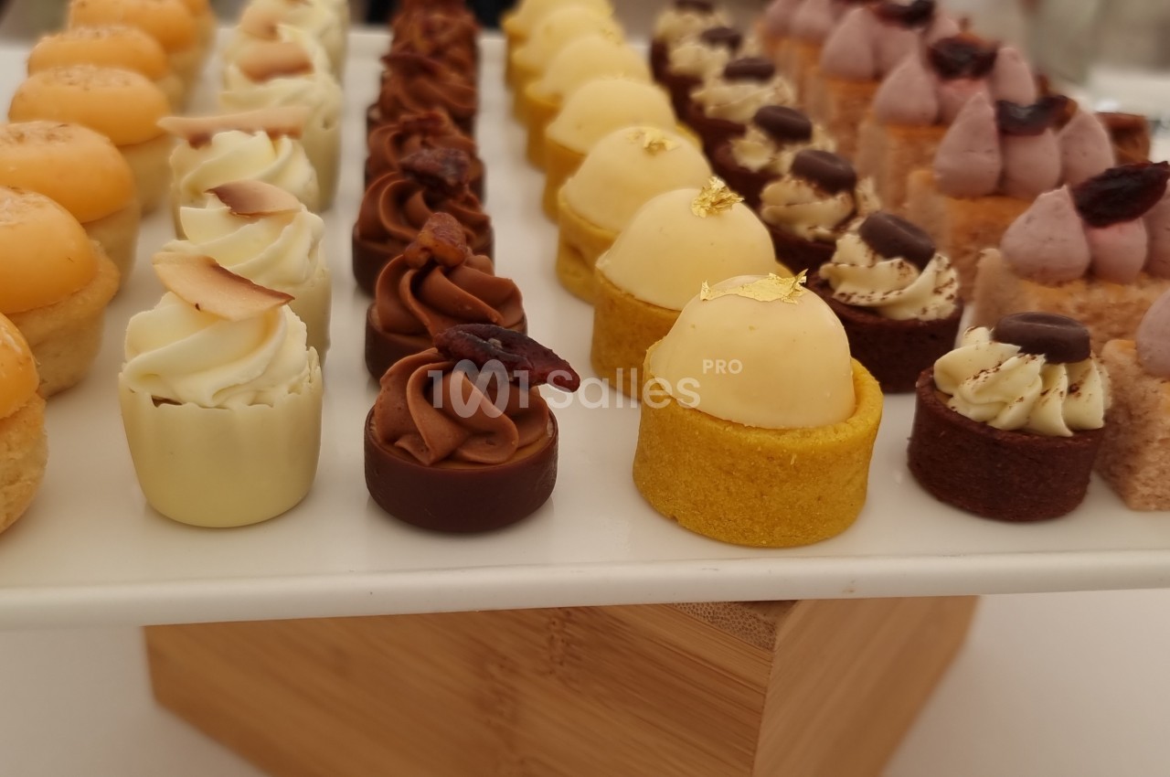 Plateau de mignardises variées disposées en rangées, comprenant des gâteaux et crèmes décorés.