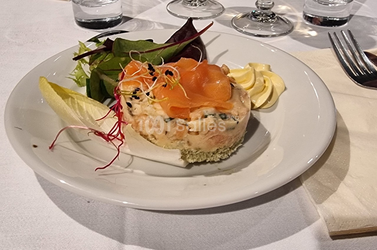 Assiette contenant un tartare de poisson garni de saumon fumé, accompagné de salade, endive et rosettes de beurre.