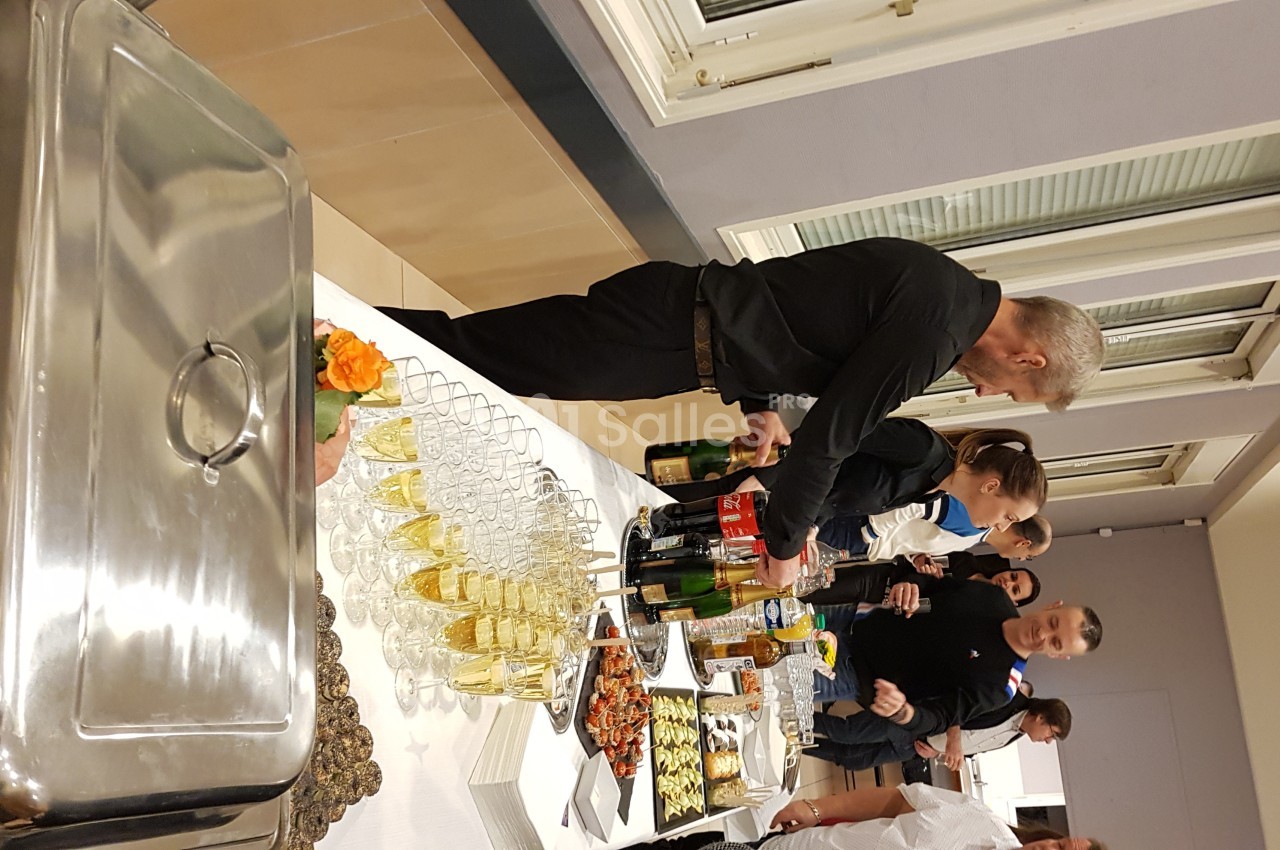 Un buffet avec des boissons, des plats variés et des convives se servant dans une salle lumineuse.