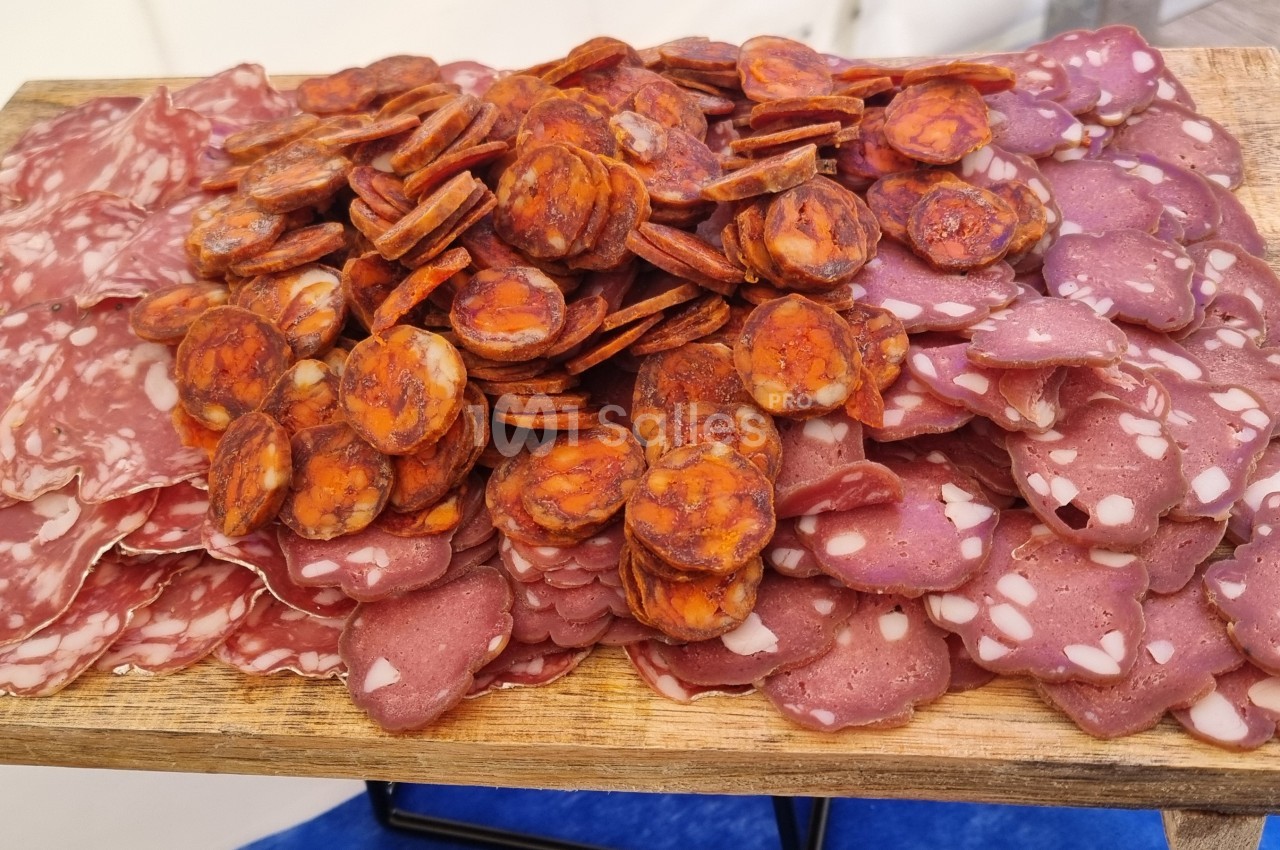 Plateau en bois garni de tranches de charcuterie variée, incluant saucisson, chorizo et saucisse sèche.