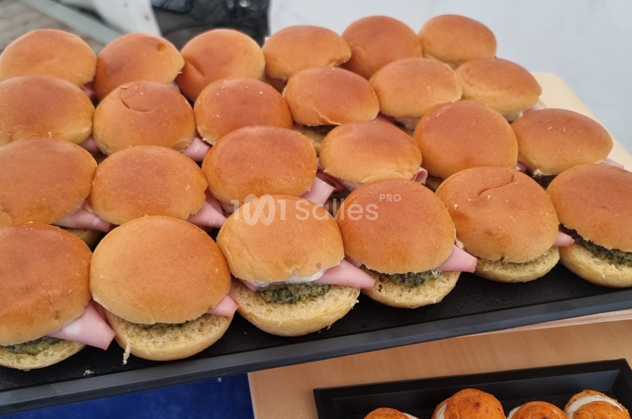 Plateau de mini-sandwichs garnis de jambon et de sauce verte, disposés sur une table en bois.