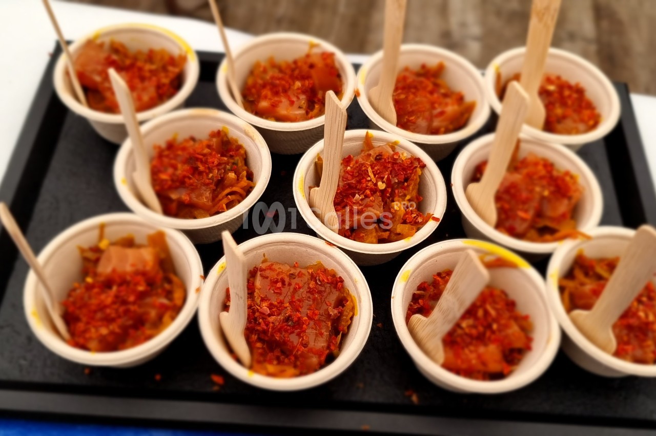Petits bols en bois remplis de tartare épicé, chacun accompagné d'une fourchette en bois, disposés sur un plateau noir.