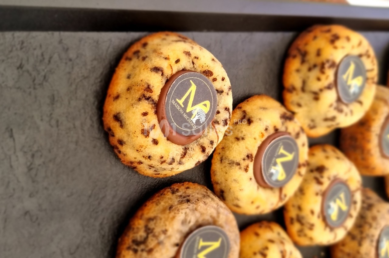 Cookies aux pépites de chocolat disposés sur un plateau noir, chacun décoré d'un disque en chocolat avec un motif doré.