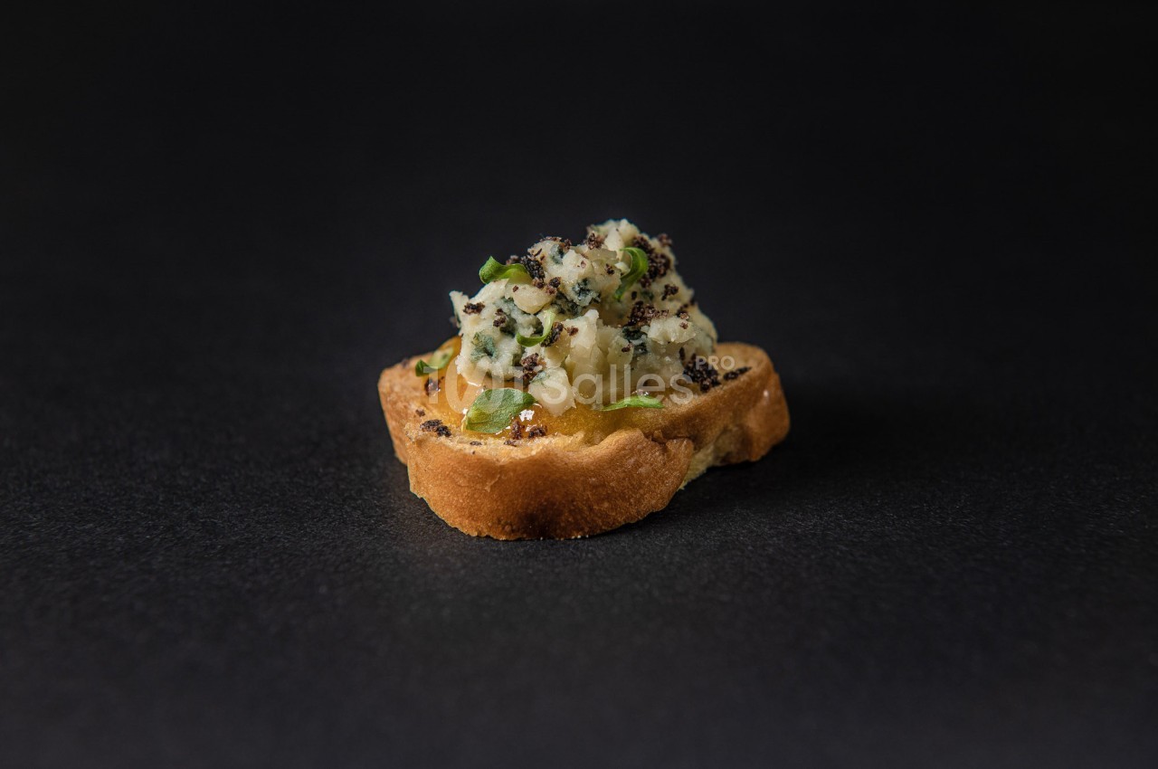 Toast garni d'une préparation crémeuse aux herbes et graines, posé sur une surface sombre.