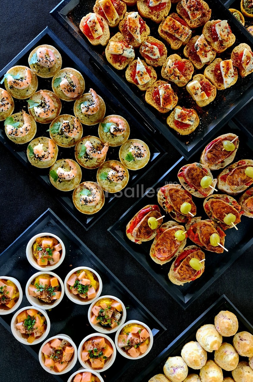 Plateaux de bouchées apéritives variées comprenant canapés, verrines et petits choux sur une table noire.