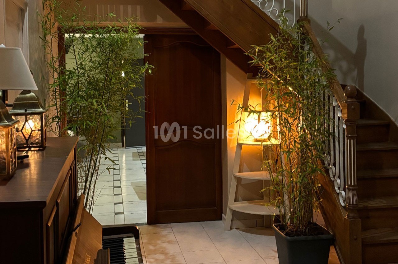 Vue d'un hall d'entrée avec un escalier en bois, des plantes en pot, un piano et un éclairage chaleureux.