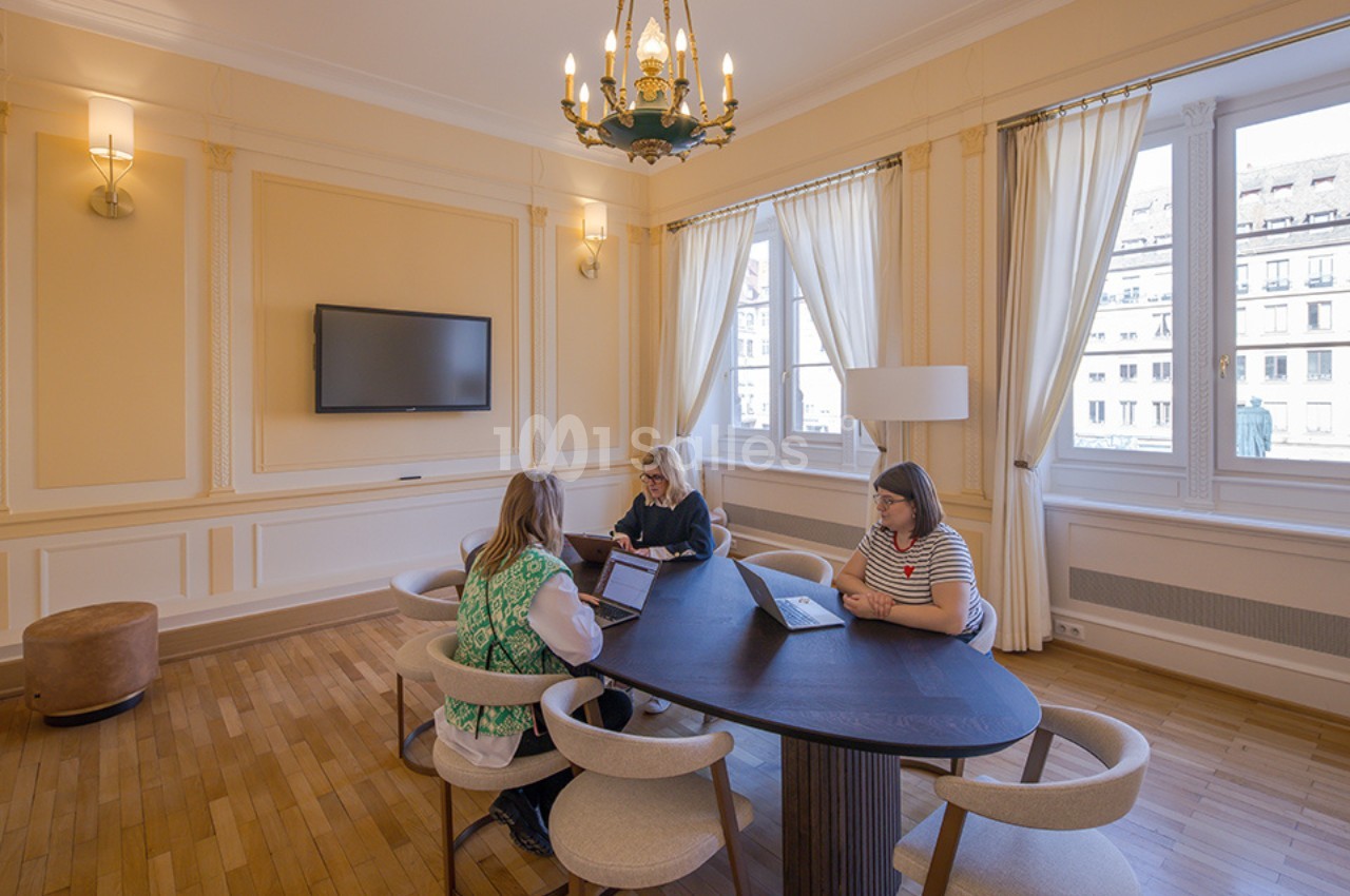 Trois personnes travaillent sur des ordinateurs portables autour d'une table ovale dans une salle lumineuse avec des…
