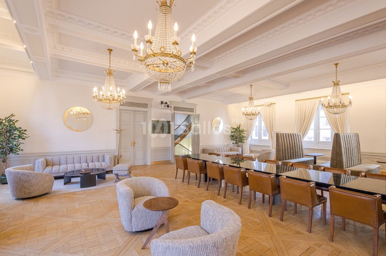 Salle lumineuse avec parquet en bois, lustres élégants, fauteuils modernes, tables et chaises en cuir disposées…