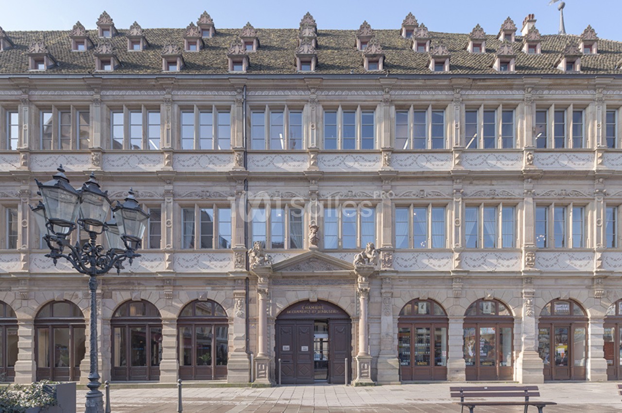 Façade d'un bâtiment historique en pierre avec des fenêtres à arcades et un toit incliné orné de lucarnes.