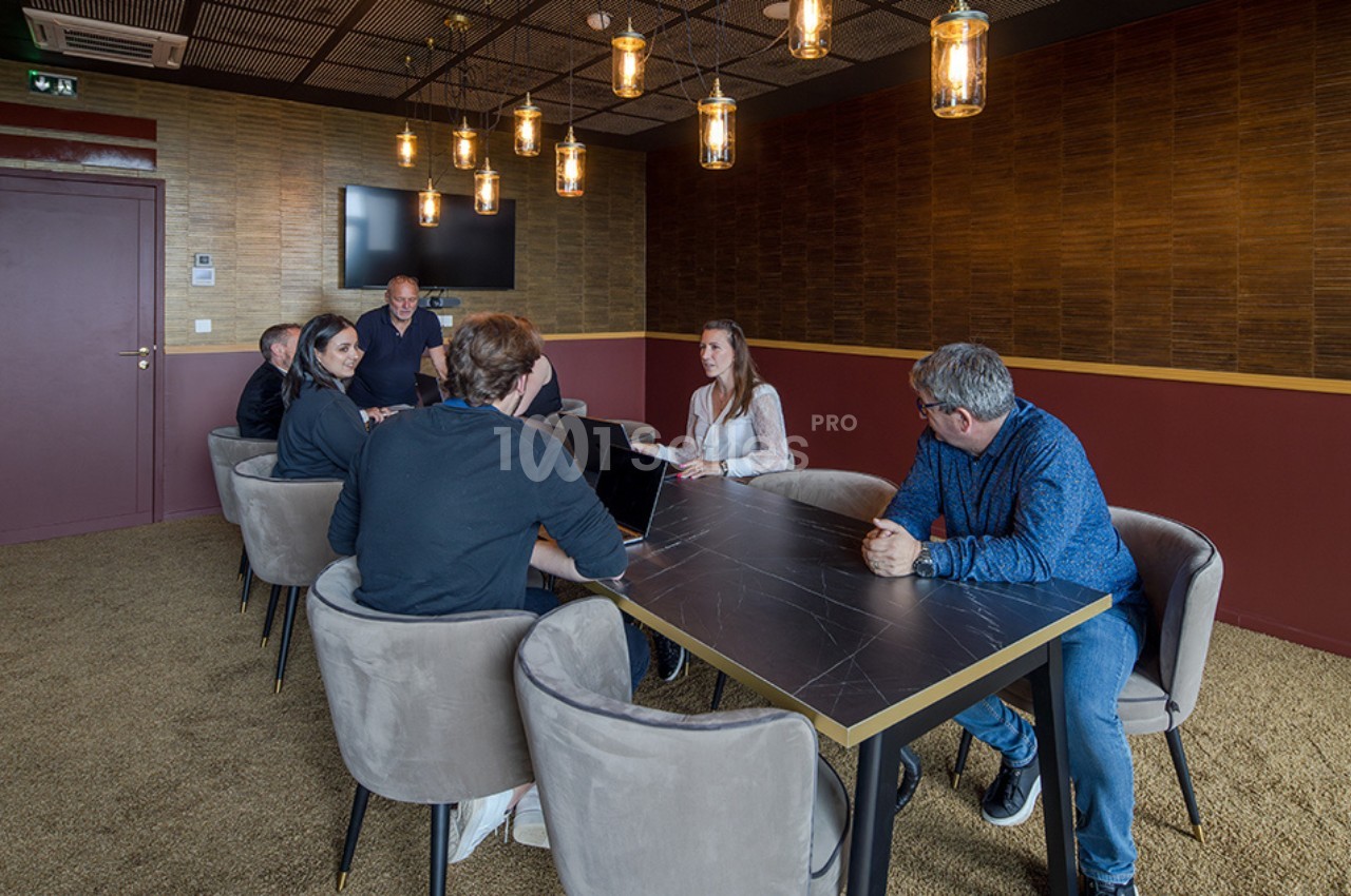 Des personnes assises autour d'une table dans une salle de réunion avec un écran mural et des luminaires suspendus.
