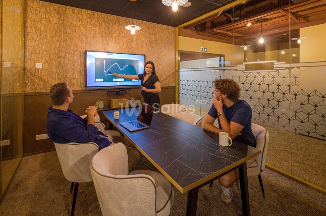 Une femme présente un graphique sur un écran à deux collègues assis autour d'une table dans une salle de réunion moderne.