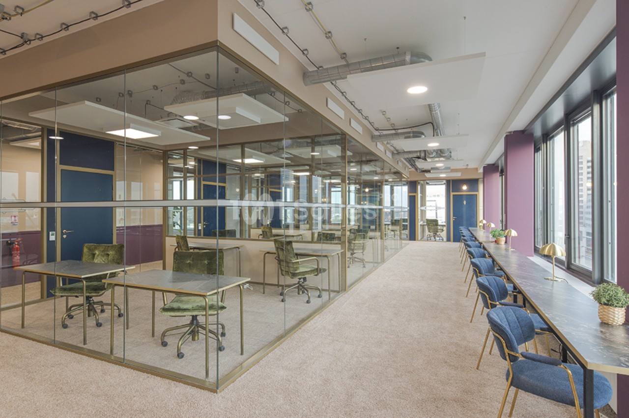 Espace de travail moderne avec bureaux vitrés, chaises vertes, et longue table avec sièges près de grandes fenêtres.