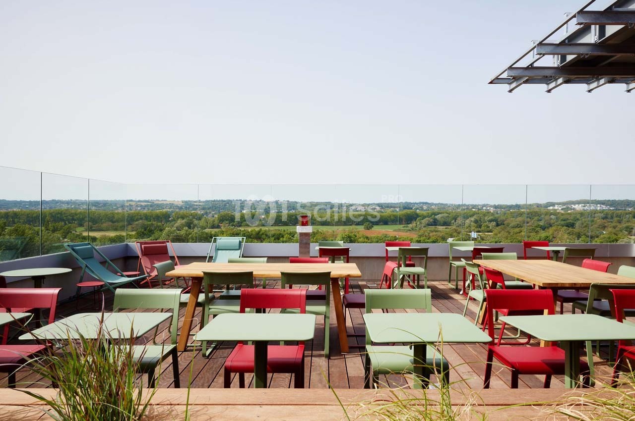 Terrasse avec des tables et chaises colorées, vue dégagée sur un paysage verdoyant à l'arrière-plan.