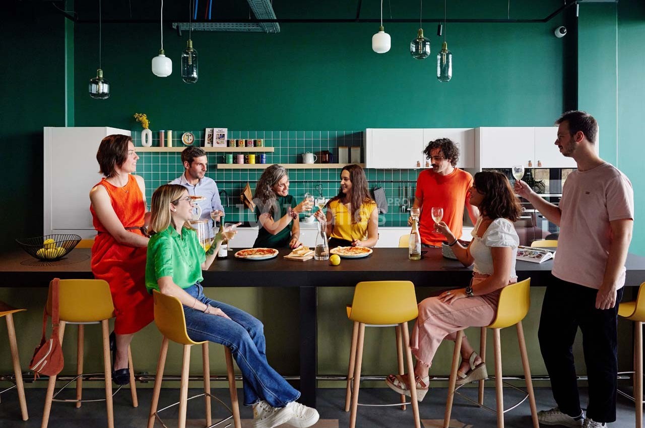 Un groupe de personnes assises et debout autour d'un comptoir dans une cuisine moderne, partageant un repas et discutant.