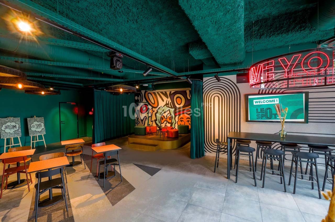 Espace intérieur moderne avec tables, chaises, mur décoré de motifs colorés et enseigne néon.