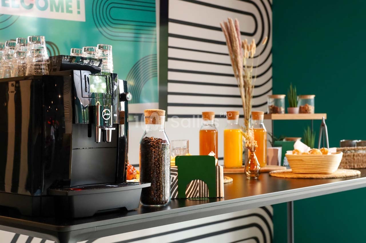 Machine à café noire et buffet avec boissons, viennoiseries et décorations dans un espace moderne et coloré.