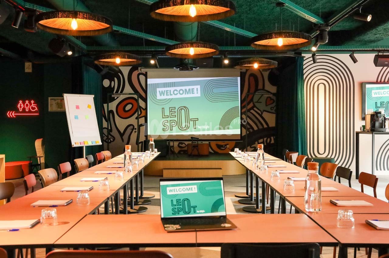 Salle de réunion moderne avec tables en U, écran de projection, tableau blanc et décorations murales colorées.