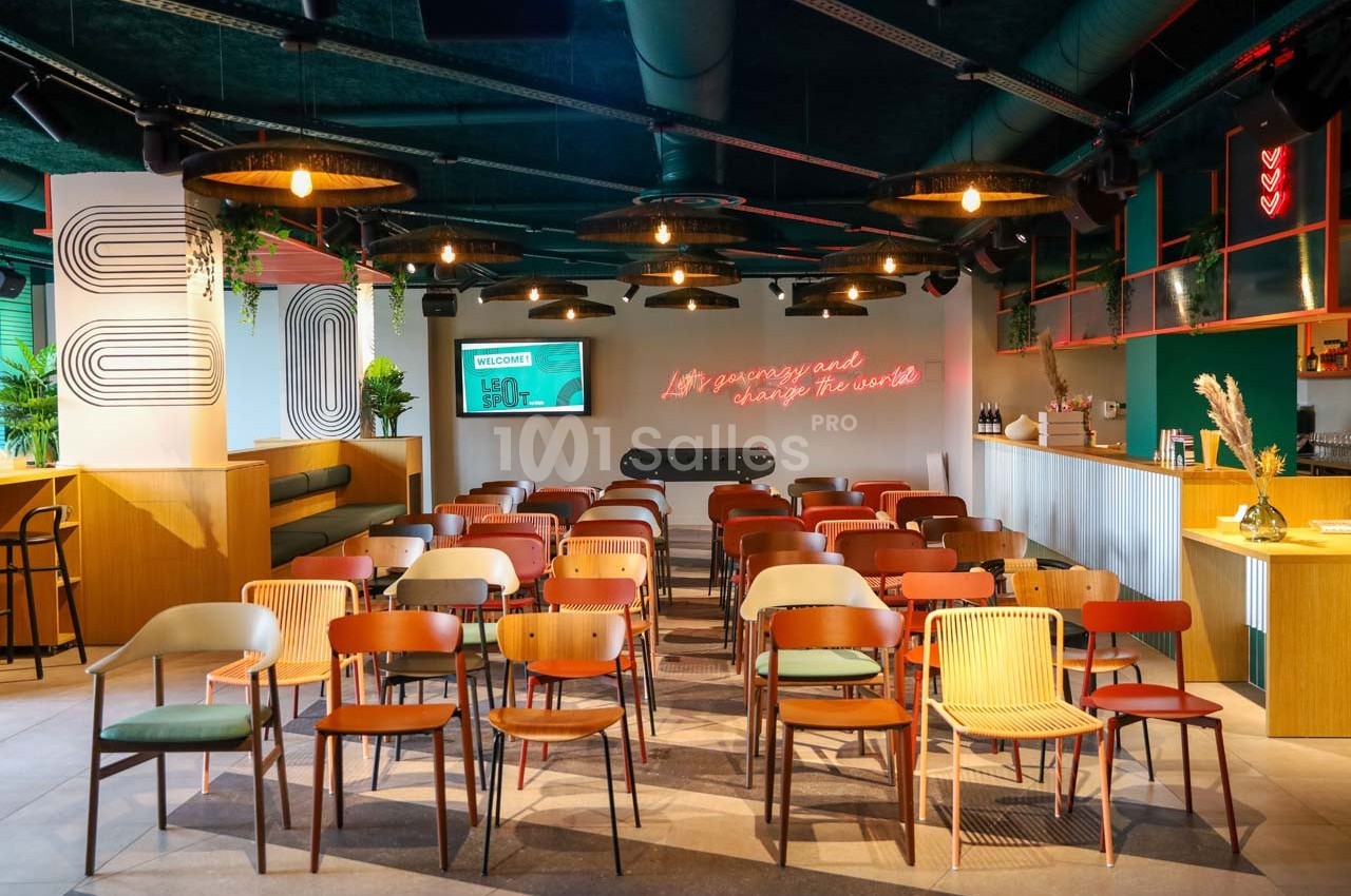 Salle moderne avec des rangées de chaises colorées, un baby-foot au centre et un éclairage chaleureux.