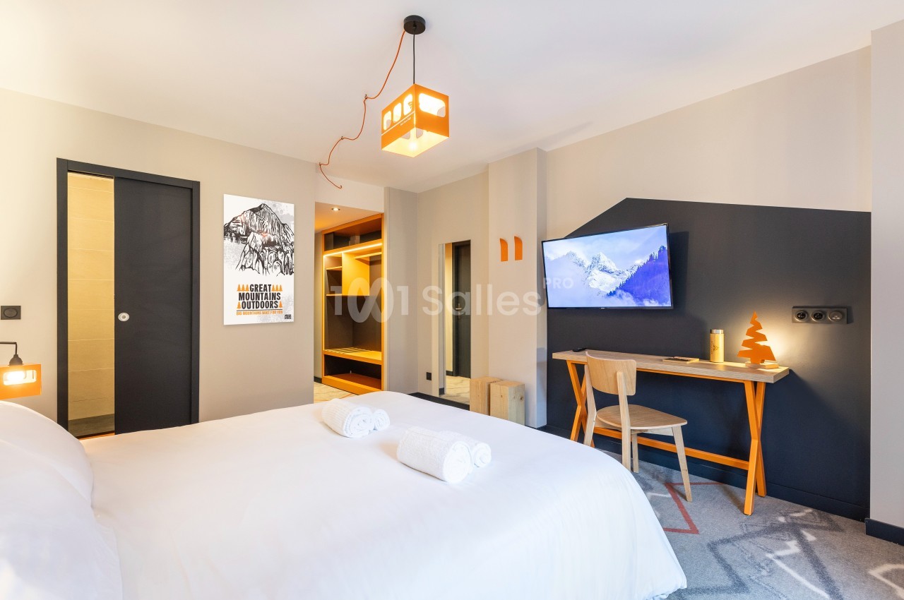 Chambre moderne avec lit double, bureau en bois, télévision murale et décoration minimaliste dans des tons clairs.