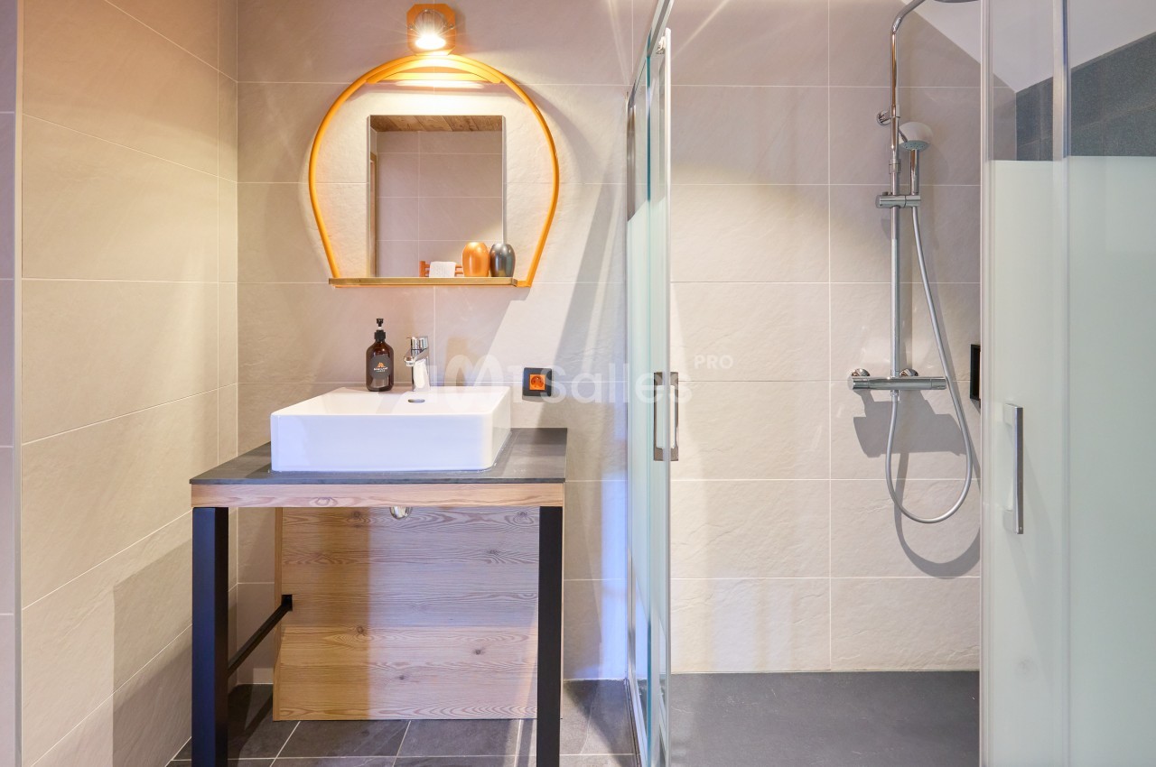 Salle de bain moderne avec lavabo sur meuble en bois, miroir rond éclairé et douche à l'italienne vitrée.