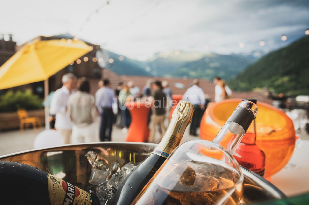Des bouteilles de vin et de champagne dans un seau à glace au premier plan, avec un groupe de personnes en arrière-plan.
