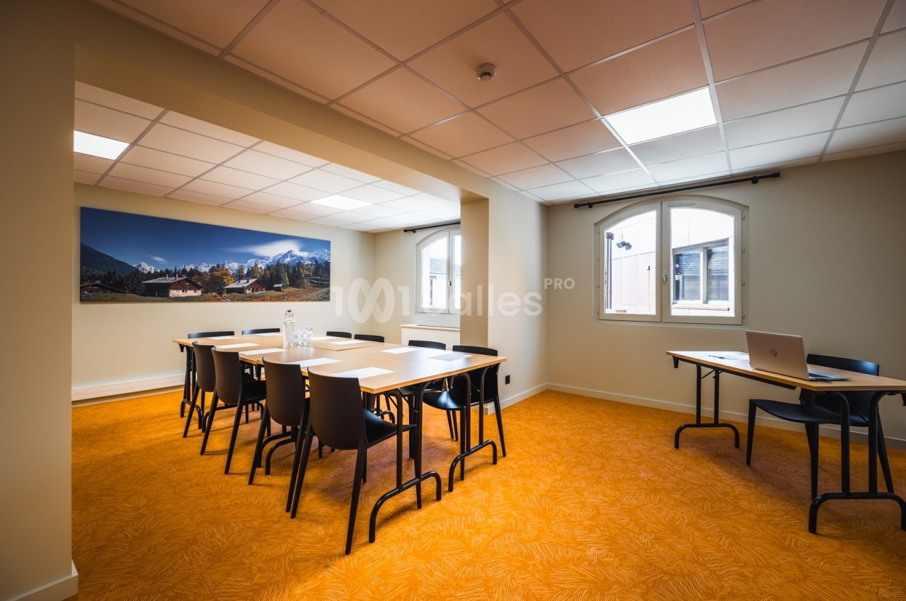 Salle de réunion lumineuse avec tables, chaises, un tableau mural et un sol orange.