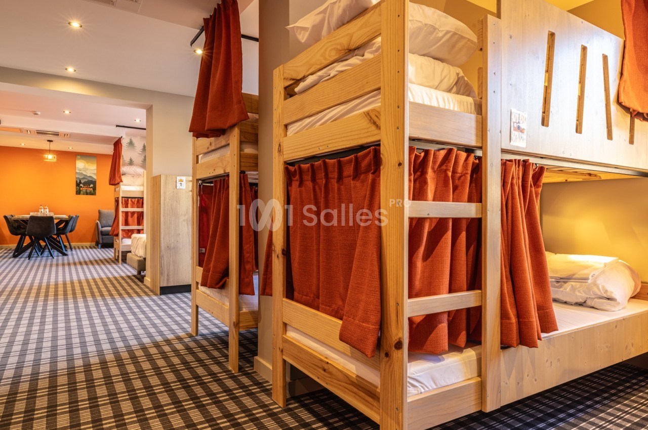 Dortoir avec lits superposés en bois, rideaux rouges pour l'intimité et sol à motif carreaux.