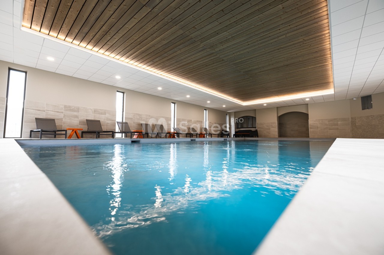 Piscine intérieure avec plafond en bois, chaises longues alignées et éclairage doux.