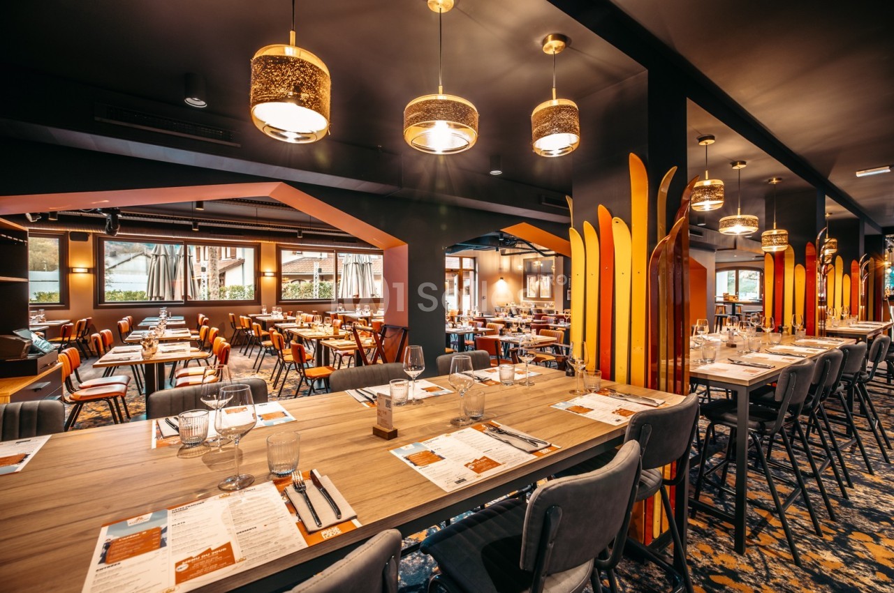 Salle de restaurant moderne avec tables dressées, chaises rembourrées et éclairage chaleureux.