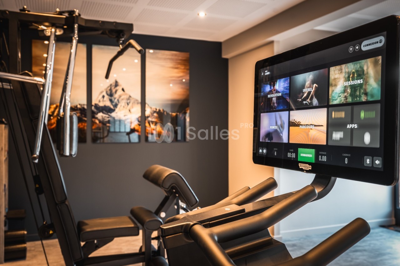 Écran tactile affichant des options d'entraînement, fixé sur un appareil de fitness dans une salle moderne avec décor mural.