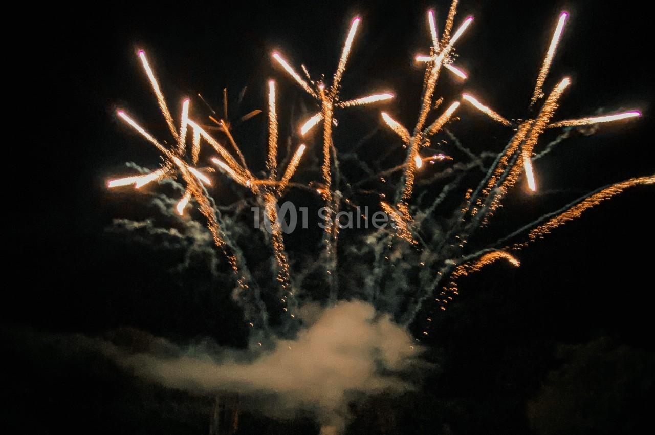 Feux d'artifice illuminant le ciel nocturne avec des traînées lumineuses et de la fumée visible en bas.