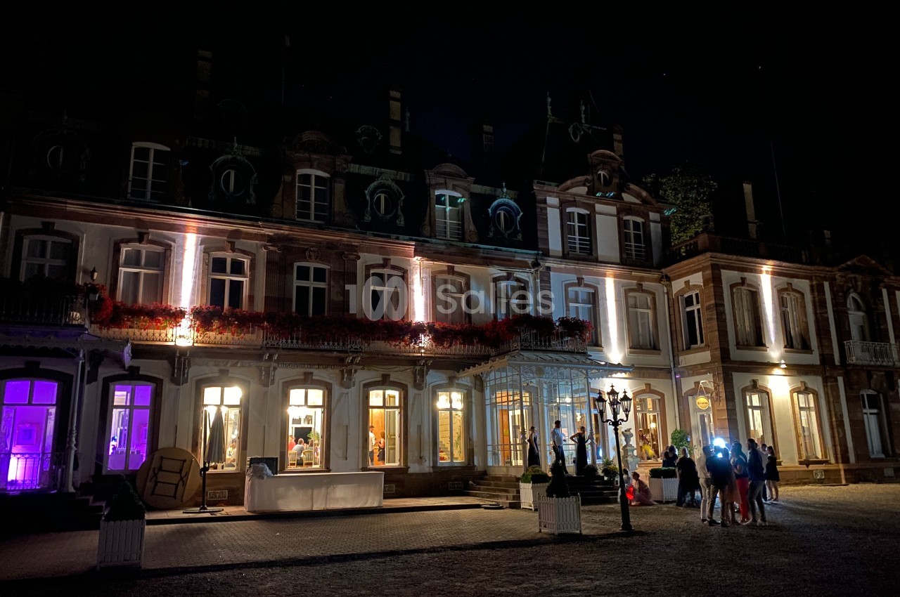 Façade d'un bâtiment éclairé la nuit, avec des lumières colorées et un groupe de personnes rassemblées devant.