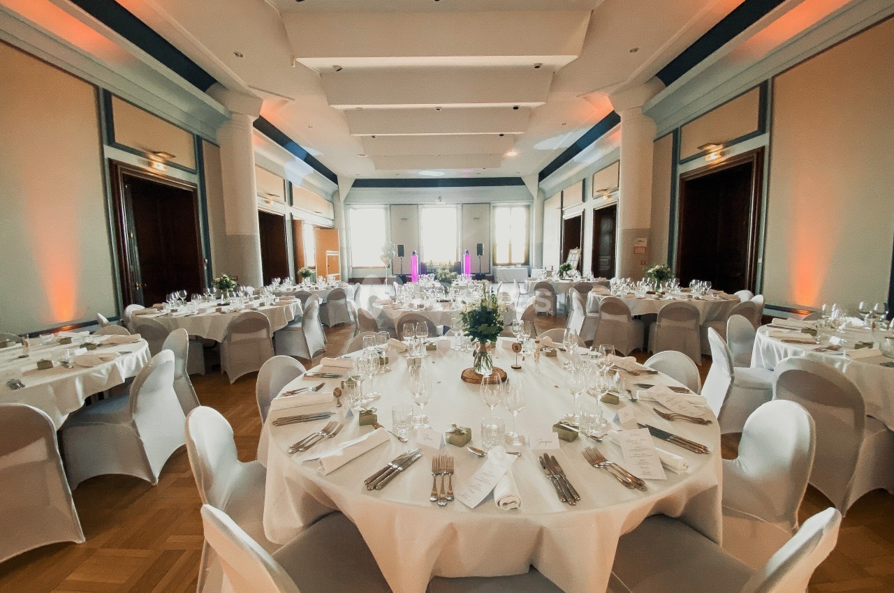 Salle de réception élégante avec tables rondes dressées, nappes blanches et éclairage chaleureux.