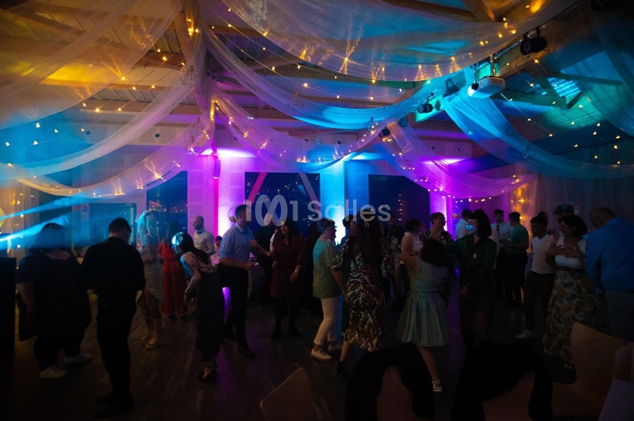 Des personnes dansent sous un plafond décoré de voilages et de lumières colorées dans une ambiance festive.