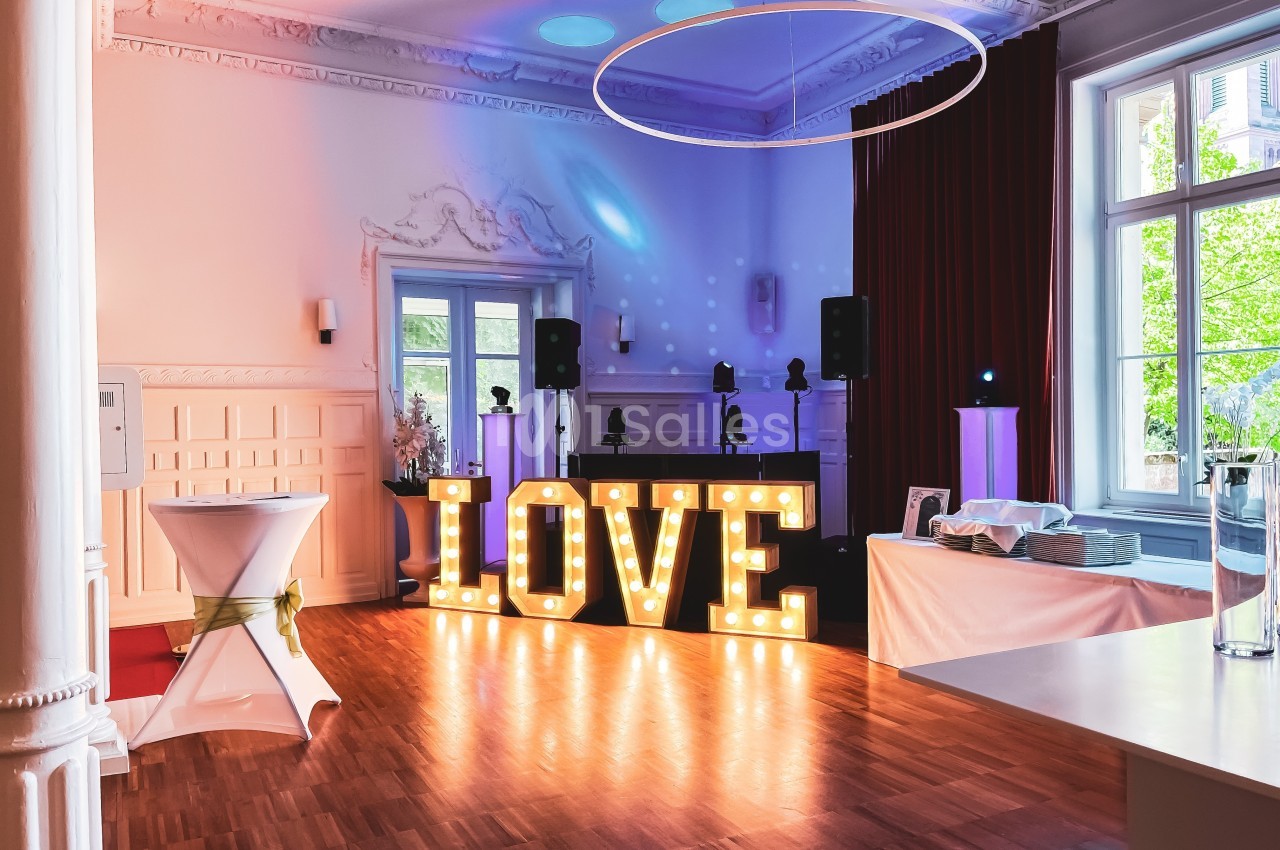 Salle de réception décorée avec des lettres lumineuses formant ’LOVE’, une table dressée et un espace DJ.