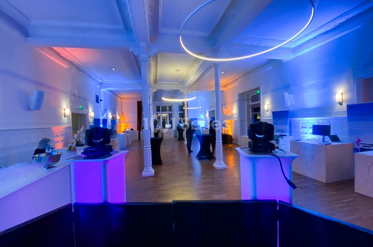 Salle lumineuse avec éclairage coloré, colonnes blanches, tables hautes et équipements techniques installés.