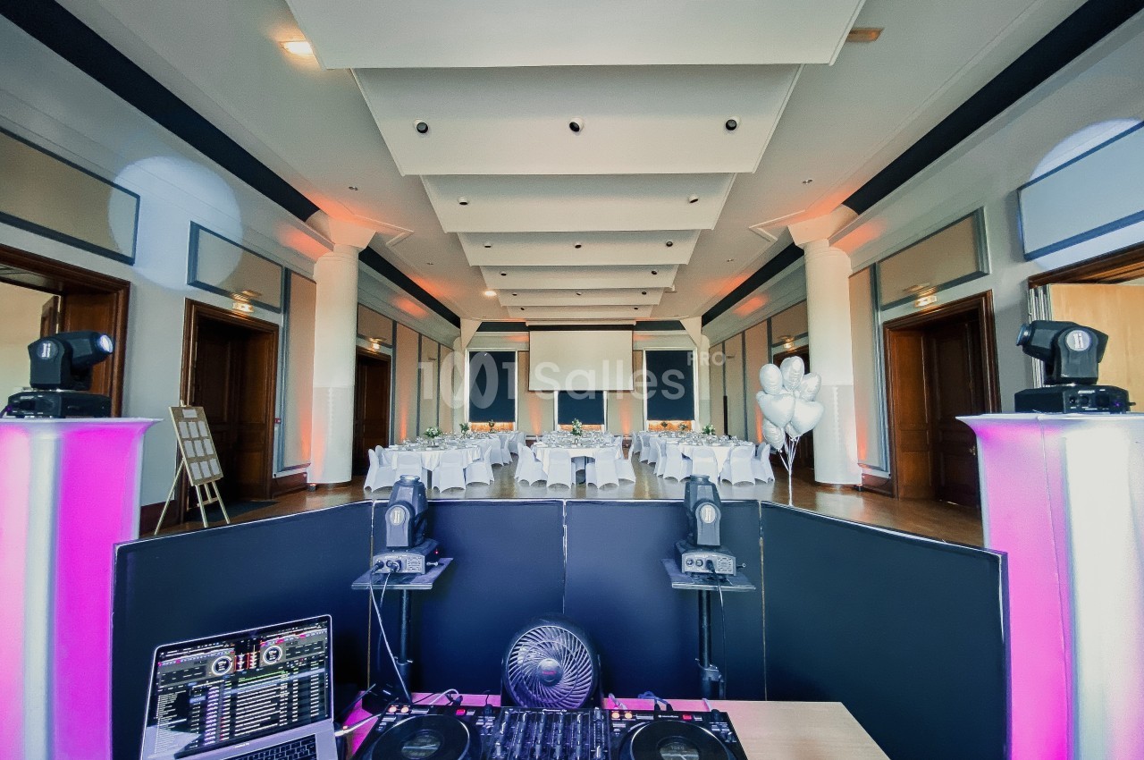 Salle de réception décorée avec des tables dressées, vue depuis une console de DJ équipée de matériel audio.