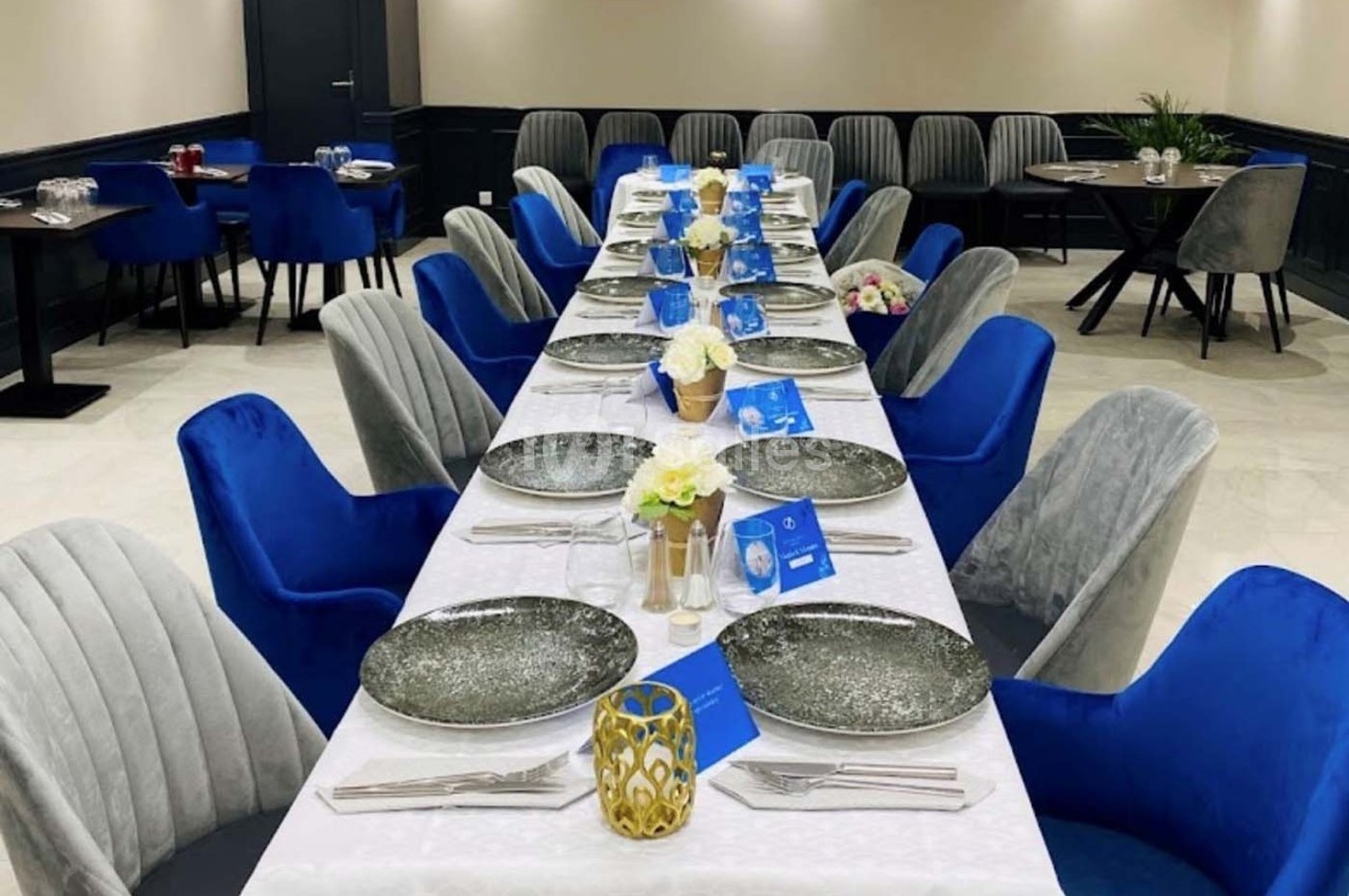 Table dressée avec nappes blanches, assiettes décoratives, fleurs et chaises bleues et grises dans une salle élégante.