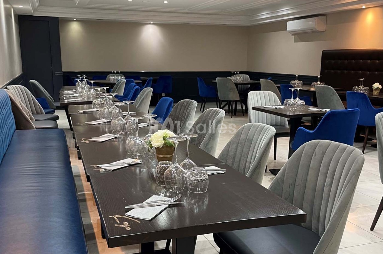 Salle de restaurant moderne avec tables dressées, chaises rembourrées grises et bleues, éclairage doux.