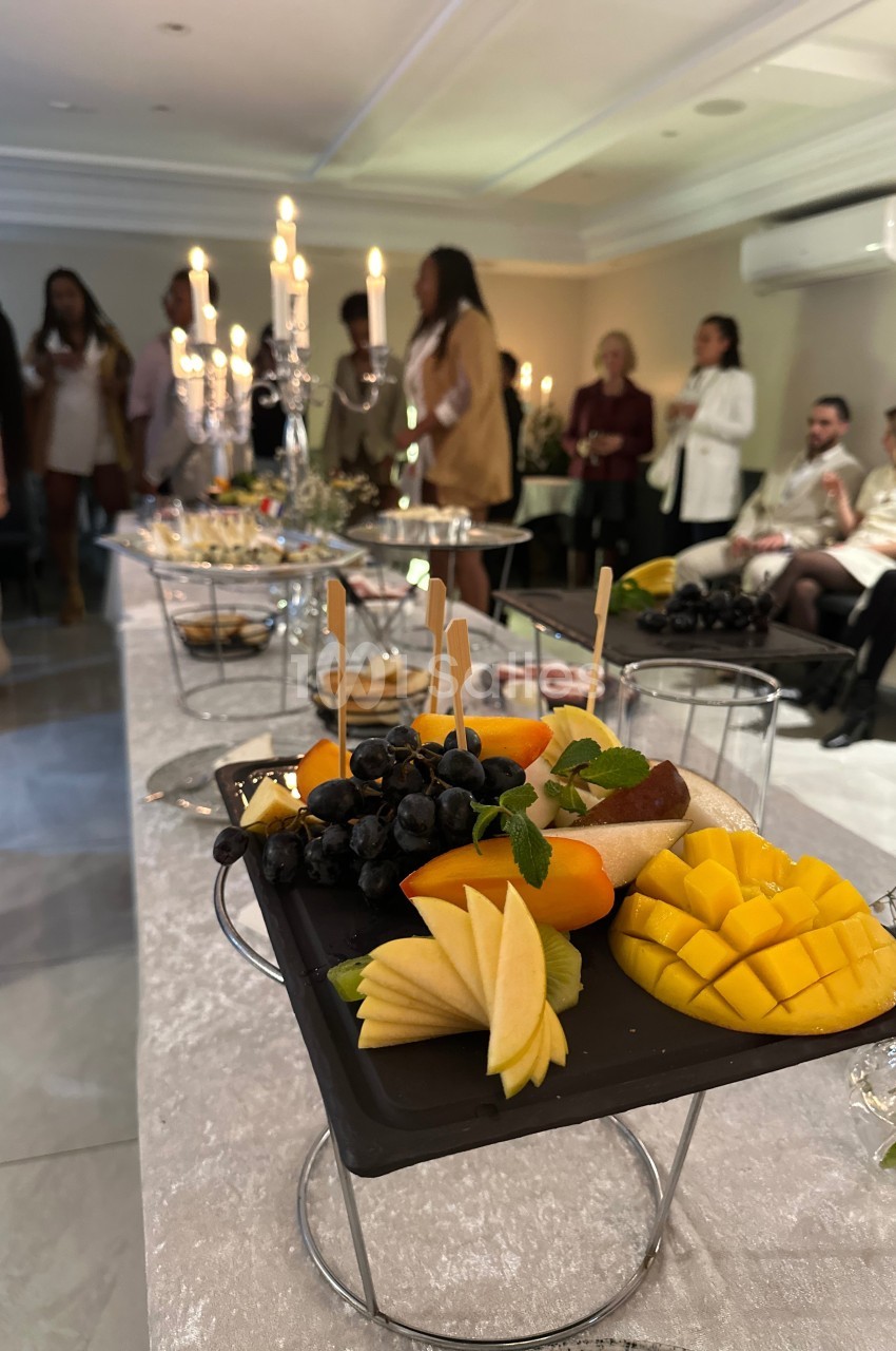 Plateau de fruits frais avec mangue, pomme, raisin et menthe, présenté sur une table lors d'un événement convivial.