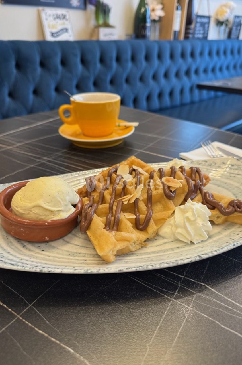 Assiette de gaufres nappées de chocolat avec boule de glace vanille et chantilly, servie sur une table de café.