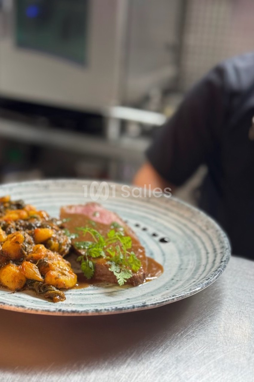 Assiette de gnocchis aux légumes et viande nappée de sauce, servie sur une table en cuisine.