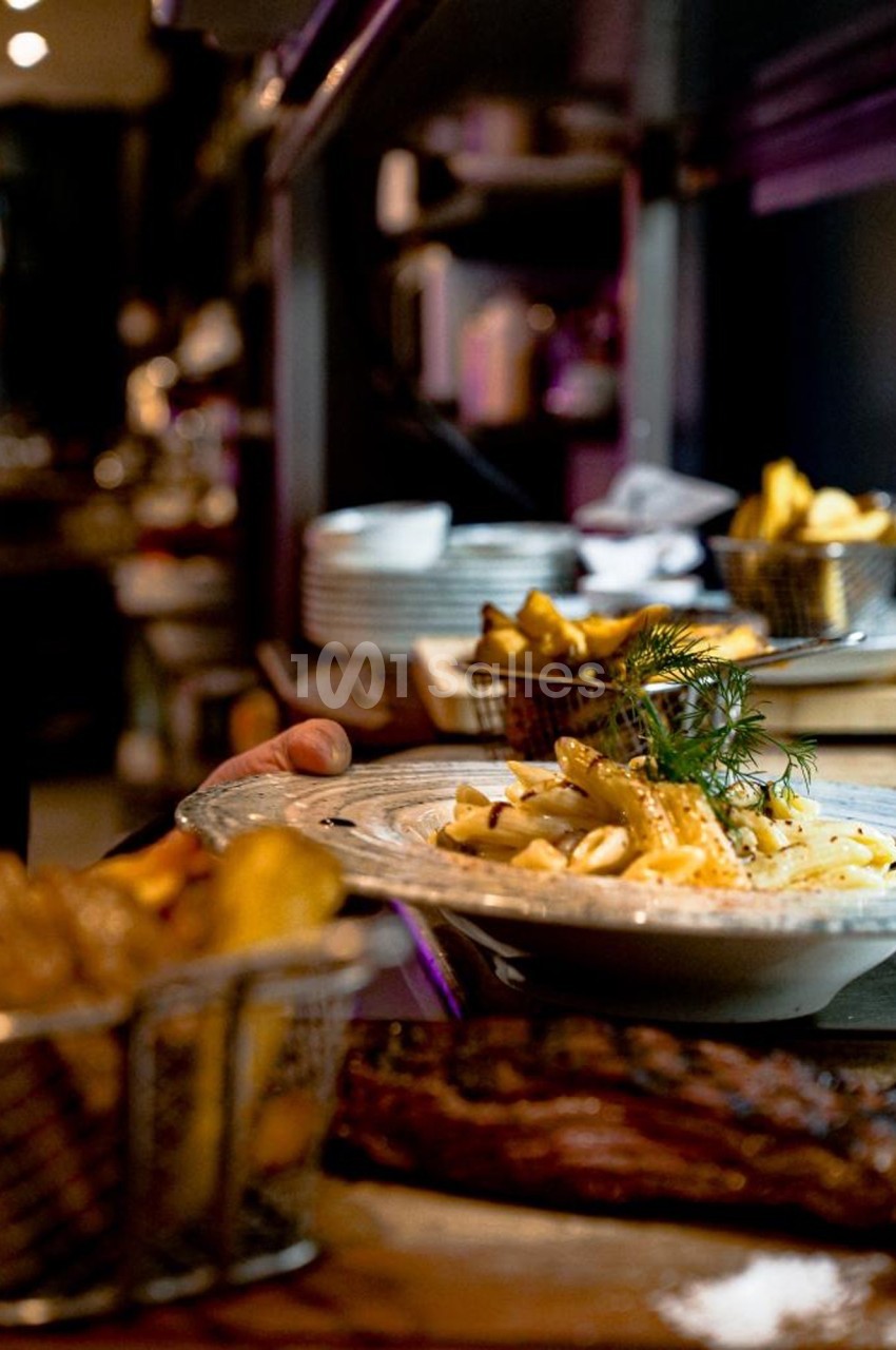 Assiette de pâtes garnie d'herbes fraîches servie avec des frites dans un restaurant à l'ambiance tamisée.