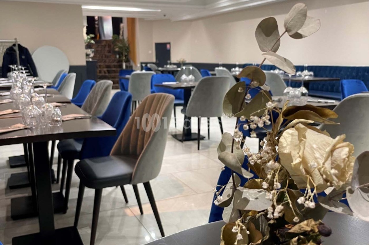 Salle de restaurant élégante avec tables dressées, chaises rembourrées et décoration florale en premier plan.