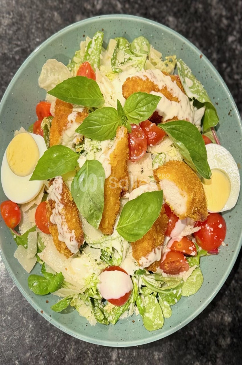 Salade composée avec poulet pané, tomates cerises, œufs durs, feuilles de basilic et copeaux de fromage.